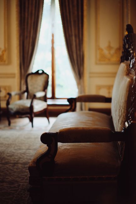 An elegant antique armchair with gold ornate wooden frame and dark blue velvet upholstery, positioned on a green sports field with artificial turf. The chair features tufted backrest and seat, with in