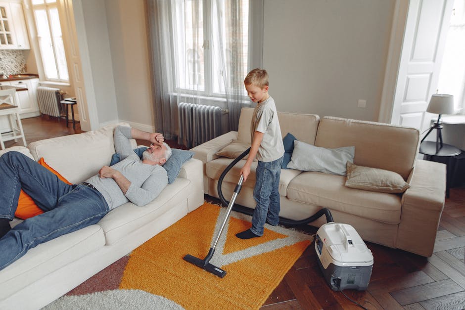 A professional cleaner from New Eltham Carpet Cleaners dressed in white protective overalls, face mask, and blue gloves performs deep carpet cleaning on a beige textured carpet within a modern, well-l